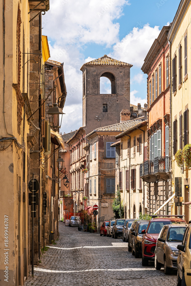 Naklejka premium Italy - Viterbo - Pianoscarano - Cobblestone street with colorful houses and bell tower in background