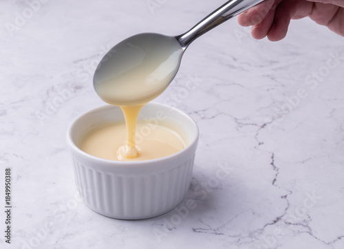 Hand pouring condensed milk in a bowl over marble background