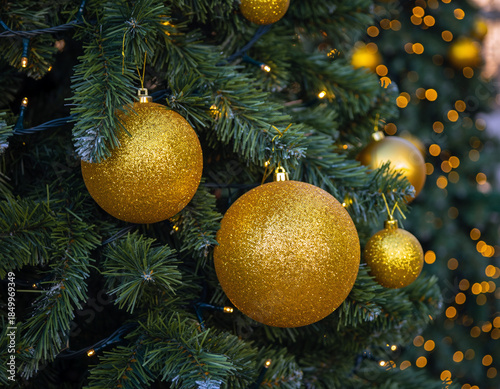 A close-up view of yellow Christmas ornaments hanging on a green-needled tree. Ai