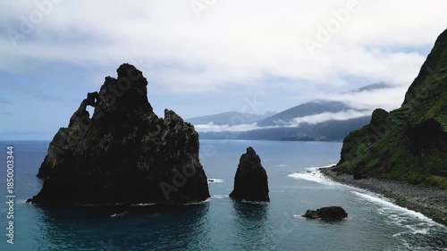 Dramatic Coastal Landscape with Towering Sea Stacks and Misty Mountains Under a Cloudy Sky.
