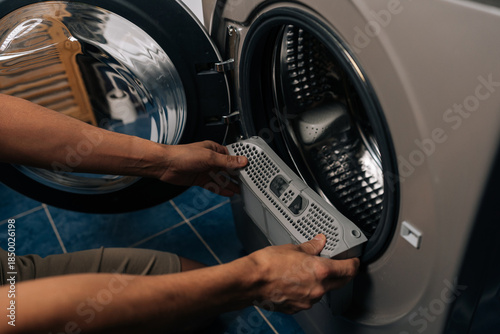 Close-up of person inspecting and removing lint filter from front-loading washing machine or tumble dryer, ensuring proper cleaning and essential appliance maintenance for optimal performance.