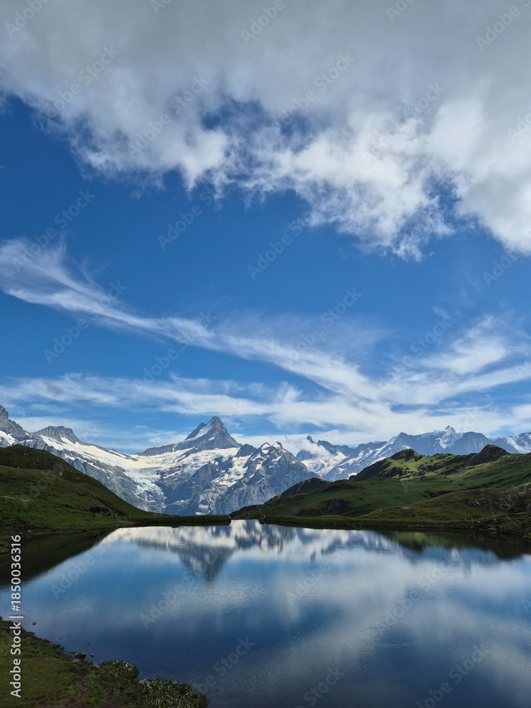 Fototapeta premium Stunning reflection of snowy alpine mountain in a calm lake under blue sky with clouds in Switzerland
