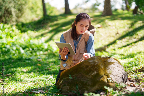 Schilderij op canvas Asian adult woman botanist conducts field research outdoors using a digital tabl