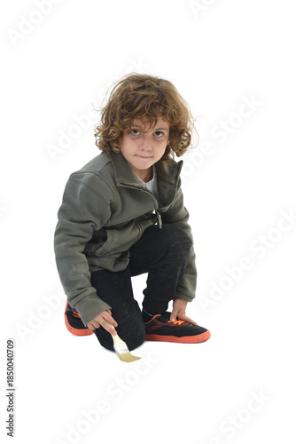 Front view of a kneeling child looking at a camera and painting with a brush on white background