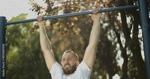 Young athlete performs pull up exercise  outdoors, street workout, slow motion, middle close up 