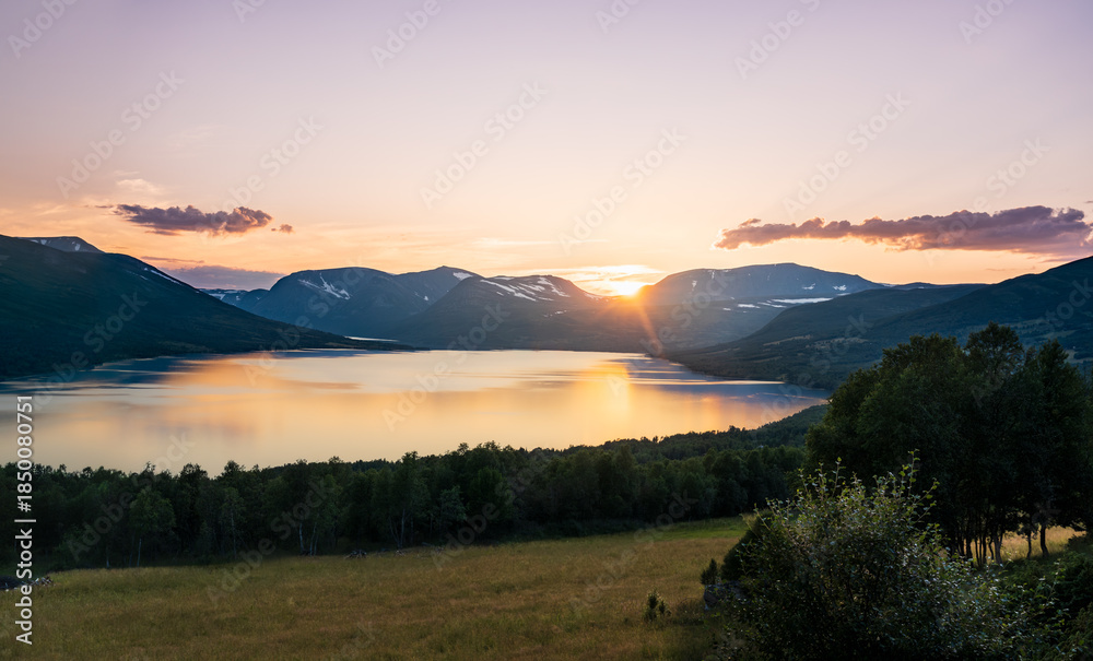 Obraz premium Sun sets over Gjevillvatnet lake. The scene shows Blåhøa and Gjevilvasskamben mountains in the Trollheimen range in Oppdal Norway. Evening light reflects on the water. 