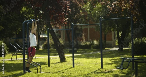 Young man performs abs exercise on bars outdoors, street workout, slow motion