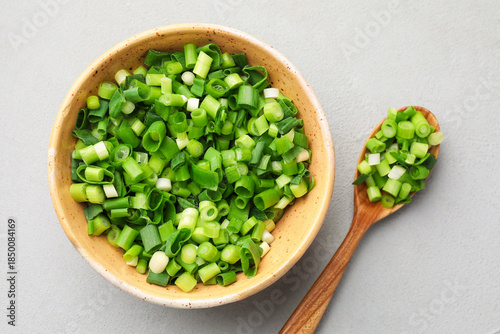 Cut green onion in bowl and spoon on grey table, flat lay