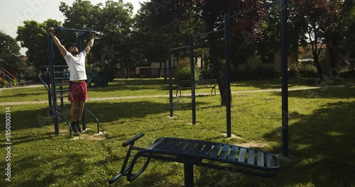 Athlete performs pull up exercise on outdoor gym equipment, street workout, slow motion