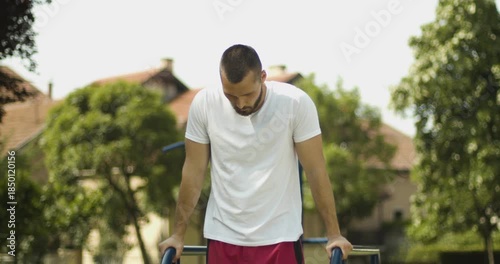 Middle close up of male athlete while working dips exercise outdoors, street workout scene