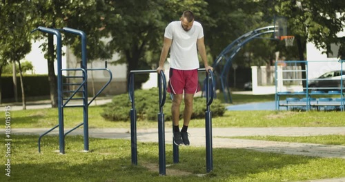 Young male fit athlete performs dips exercise outdoors, street workout, slow motion
