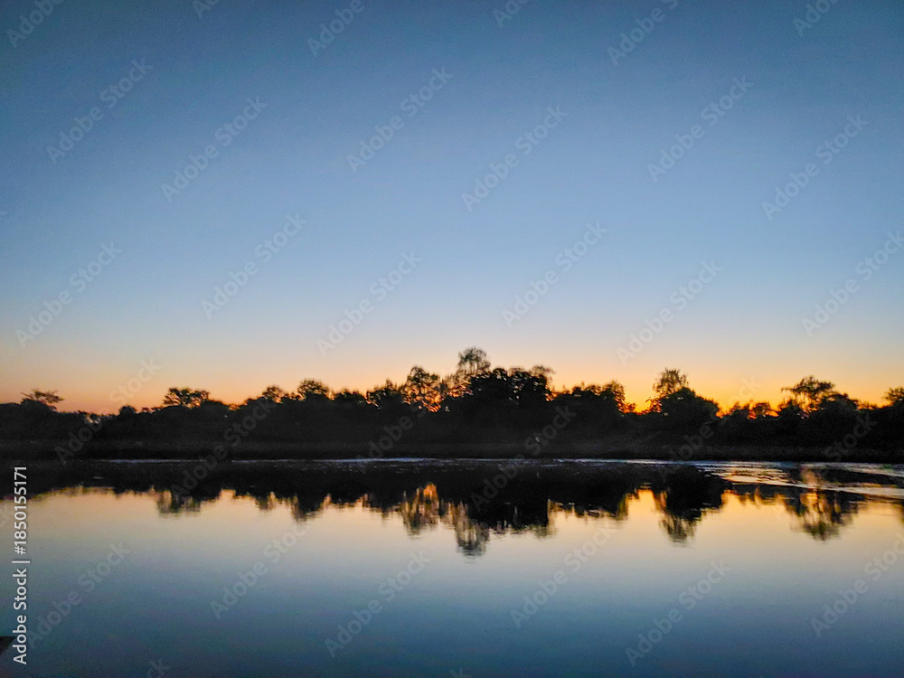 Obraz premium Calm Sunset Over Lake With Tree Silhouettes and Reflection