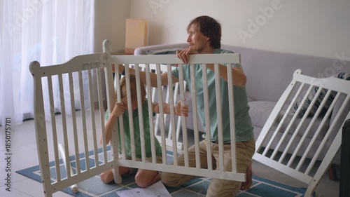 Father and son assembling a baby crib together for their soon arriving son and brother. Family teamwork, bonding, parenting support and preparation for newborn concept.