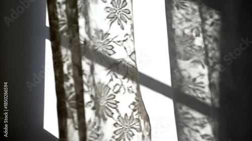 Sunlight streams through floral curtains creating shadows on a bright wall.