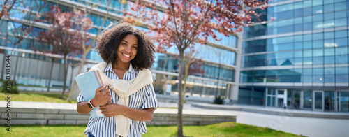 Banner for ads. Happy pretty female African American girl student standing outside university holding notebooks looking at camera outdoor, portrait. Applying university, admission scholarship program.