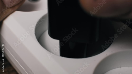 Macro shot of a black European plug with metal prongs inserting into white plastic socket holes. This connects a device to the power supply ensuring a secure electrical connection.