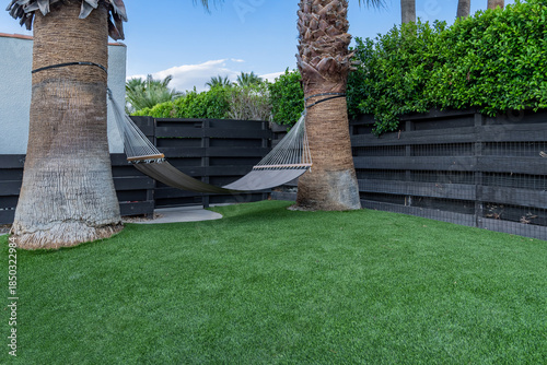 Hammock between two large palm trees, artificial grass, in backyard