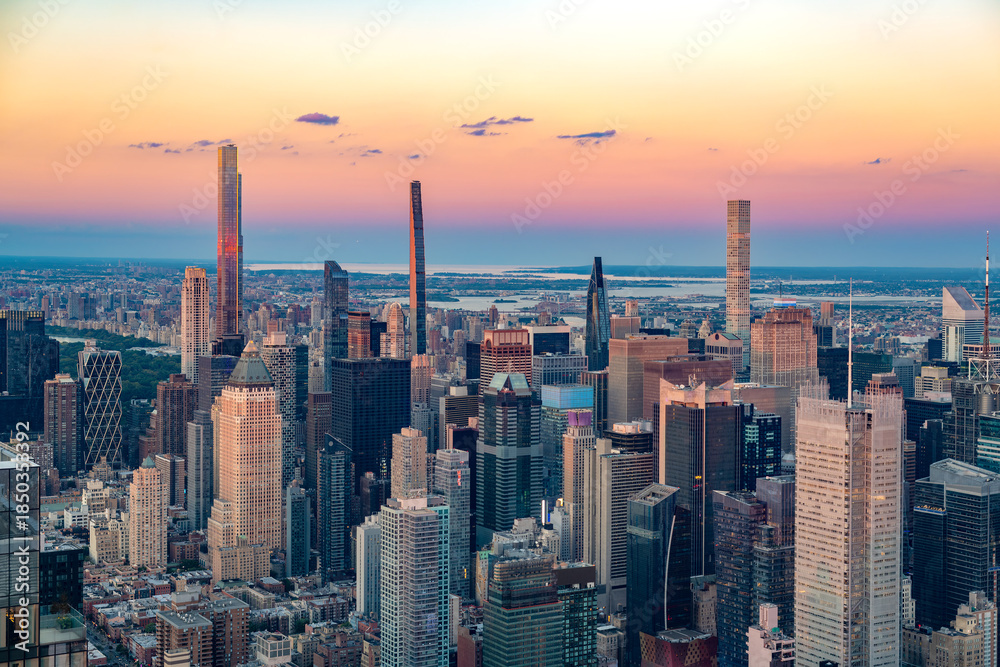 Fototapeta premium The iconic Billionaires Row skyscrapers rise above the dense Midtown Manhattan skyline during a vibrant sunset.