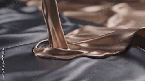 A stream of rich, melted chocolate or caramel pouring onto luxurious dark satin fabric, creating smooth ripples.