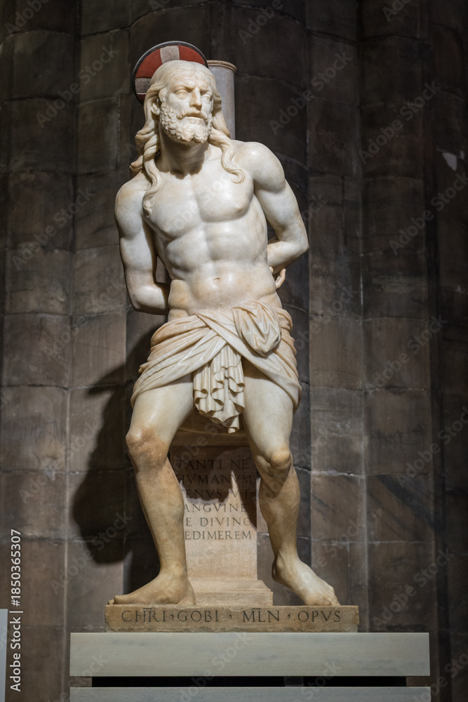 Obraz premium Milan, Italy - December 14, 2025: Marble statue of Christ bound before the Passion inside Milan Cathedral (Duomo di Milano), illuminated against dark stone columns.