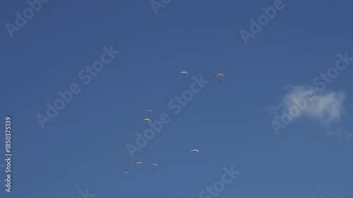 Group of colorful paragliders soaring through a clear blue sky flying next to the cloud captured in 4K