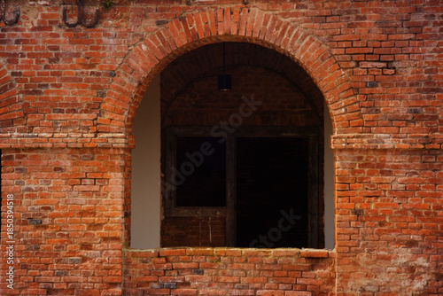 Old window facade, with curved design made of red brick. Window with trellis in old brick wall.
