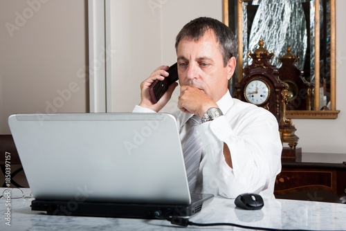 Businessman Working on Laptop While Talking on Phone