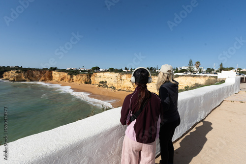 A mother and daughter enjoying the beautiful view Yellow rocks and cliffs on the sandy beach. A cove by the sea, Our Lady of the Rock, Praia Nova, Lagos. Algarve, Portugal