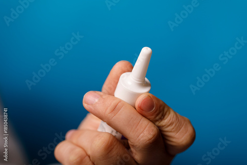 Fotografie Close-up of a hand holding a white nasal spray bottle against a bright blue background