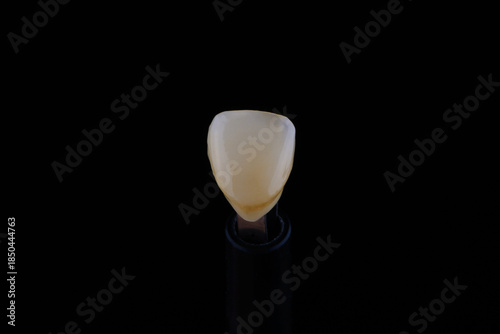 Close up shot ultra thin dental zirconium crown is held with tweezers with black background.