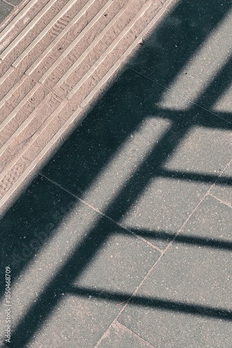 Strong geometric shadows cast across urban pavement, creating an abstract pattern of light and dark in a minimalist city scene.