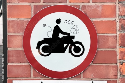 Traffic sign prohibiting motorcycles mounted on a brick wall, vandalized with graffiti, blending urban regulation and street culture.
