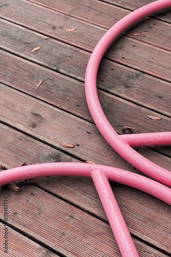 Curved pink metal bars resting on a weathered wooden deck, creating a minimalist abstract composition with texture and soft color contrast.