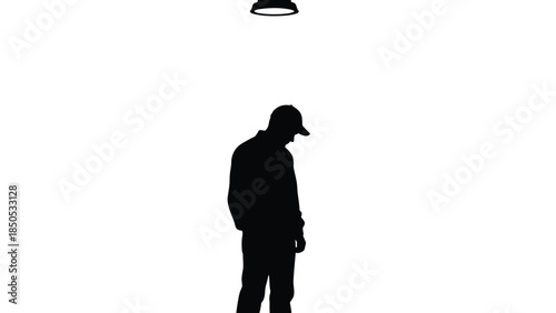 Silhouette of a man wearing a baseball cap standing alone under a harsh overhead light source