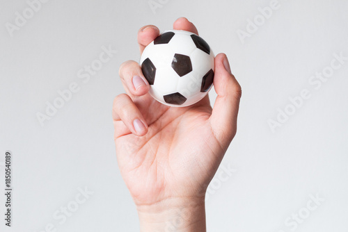 Hand lifting a small soccer ball on a neutral background, concept of healthy habits and sports therapy