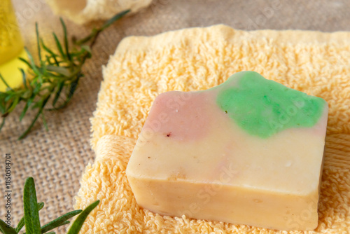Handmade soap from natural ingredients rosemary essential oil, on yellow towel with fresh rosemary twig and loofah. Concept of sustainable use, bath products. Flat lay