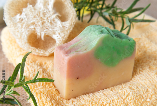 Handmade soap from natural ingredients rosemary essential oil, on yellow towel with fresh rosemary twig and loofah. Concept of sustainable use, bath products. Flat lay