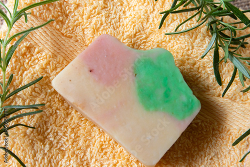 Handmade soap from natural ingredients rosemary essential oil, on yellow towel with fresh rosemary twig. Concept of sustainable use, bath products. Flat lay