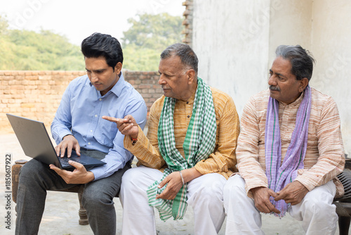 Senior rural Indian people sitting with insurance agent showing plans on laptop. Bank manger explain government loan scheme to village farmers.