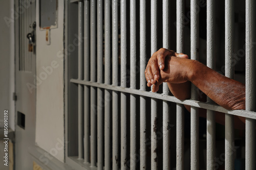 Close up view of hands behind bars in a prison cell, symbolizing incarceration and the criminal justice system.