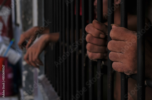 Canvas-taulu Close up view of hands behind bars in a prison cell, symbolizing incarceration and the criminal justice system