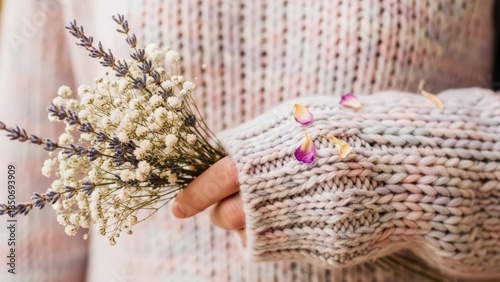 Close-up of a person in a knitted sweater holding a delicate bouquet of white heather flowers.