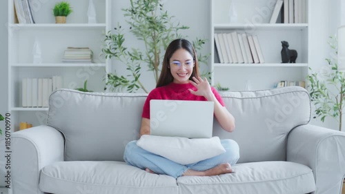 Happy young Asian woman using laptop while seated on couch at home
