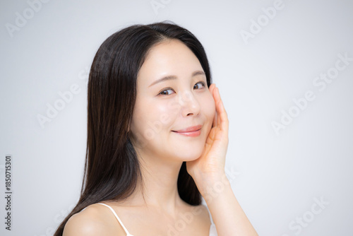Japanese woman with hand on cheek smiling, radiant skin, clean-cut portrait, camera gaze