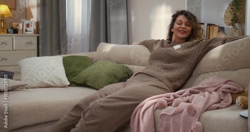 Shot of a couch as family members sit down one by one, hugging and relaxing together at home. Their dog joins them, creating a calm, happy family moment in a modern living room.