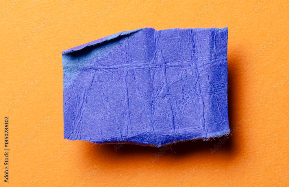 Fototapeta premium One single blue torn ripped wrinkled crumpled blank paper note with drop shadow, folded edge and copy space for text on orange background
