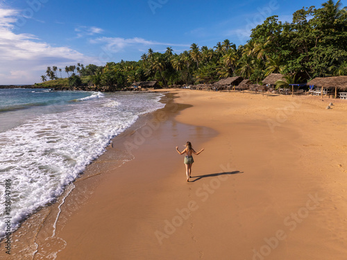Young Woman Walking on Golden Sand Beach with Thatched Beach Huts, Goyambokka Beach, Sri Lanka