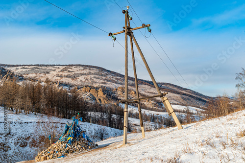 Hölzerner Strommast mit Überlandleitung in menschenleerer, mongolischer Winterlandschaft und einem sog. 