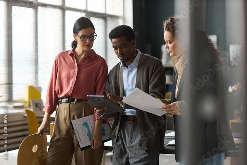 Photos Caucasian women and Black man collaborating in modern office, reviewing document
