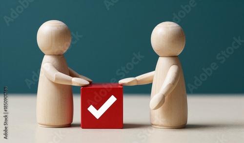 Two wooden figures jointly hold a red checkmark cube, symbolizing teamwork and successful collaboration.